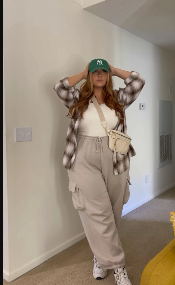 A plus size woman wearing White tank top
Plaid button-up shirt (open)
Beige cargo sweatpants
Green NY baseball cap
Cream crossbody bag
White sneakers