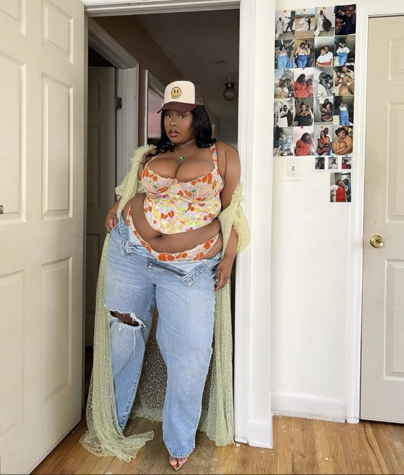 A plus size woman wearing Floral print mesh crop top Light-wash ripped baggy jeans Light green sheer mesh duster cardigan Trucker hat with smiley face Gold pendant necklace