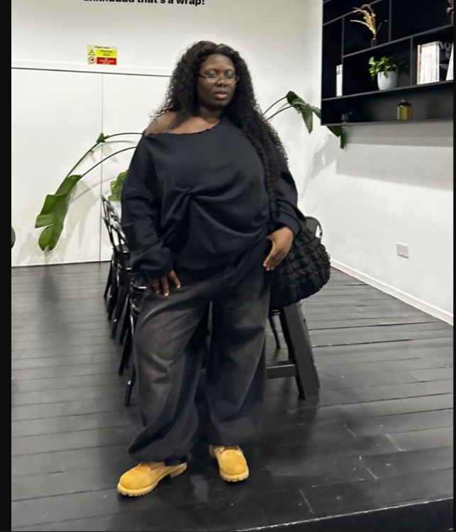 A plus size woman wearing Black off-shoulder long-sleeve top Black wide-leg pants Yellow suede chelsea boots Black woven tote bag