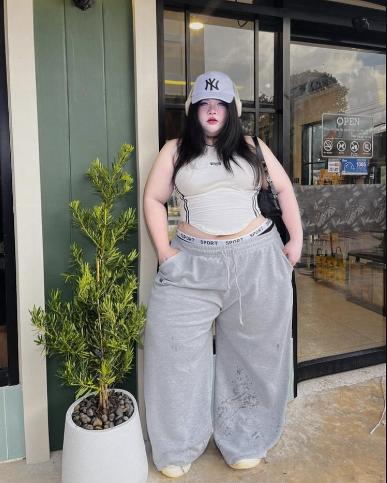 A plus size woman wearing White ribbed tank top Grey sweatpants with white waistband detail White NY baseball cap Black crossbody bag White sneakers