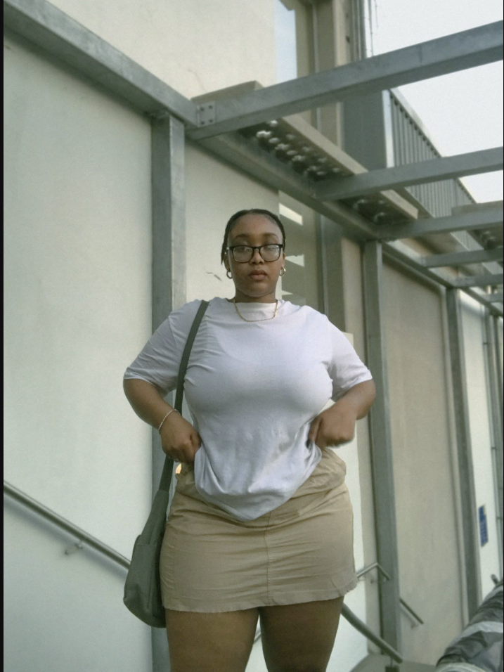 A plus size woman wearing White short-sleeve t-shirt Beige mini skirt Green shoulder bag Gold necklace Hoop earrings