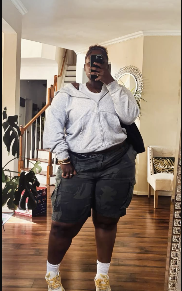 A plus size woman wearing Grey zip-up hoodie
White t-shirt
Camouflage cargo shorts
White crew socks
Yellow and white sneakers