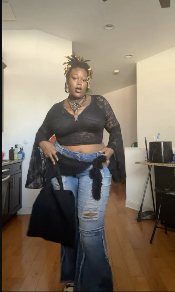 A plus size woman wearing Black lace bell sleeve crop top Blue ripped flared jeans Black fabric tie belt