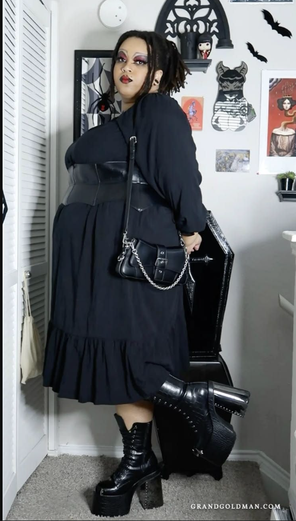 A plus size woman wearing Black long sleeve midi dress Wide black leather waist belt Black platform combat boots Black chain-strap handbag