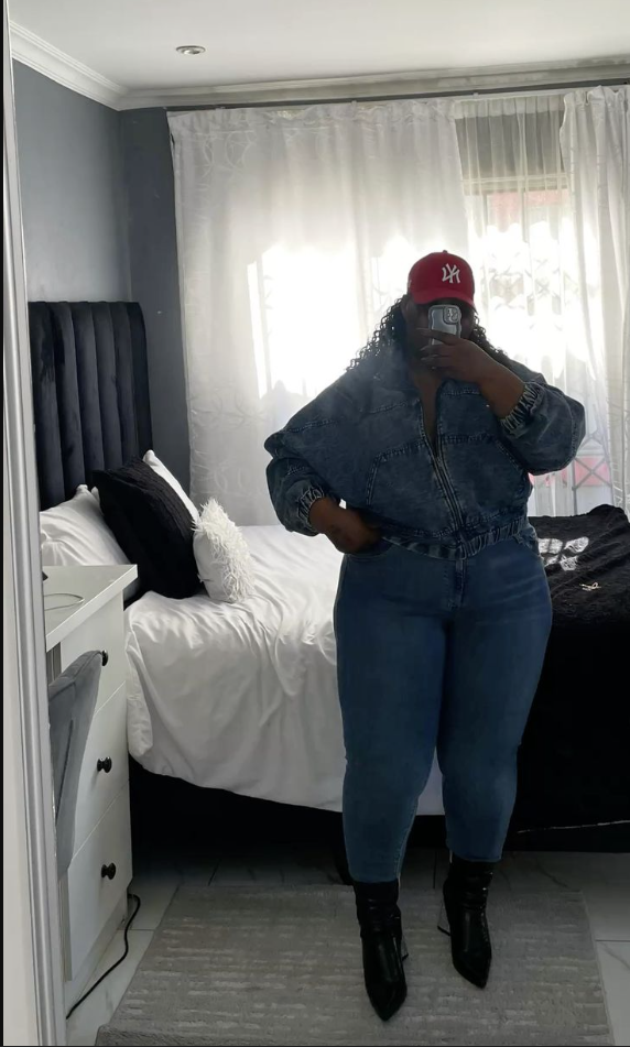 A plus size woman wearing Red NY baseball cap Blue denim zip-up jacket Blue high-waisted jeans Black pointed toe ankle boots