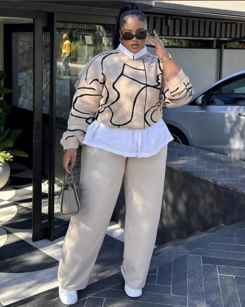 A plus size woman wearing Beige abstract print sweater White button-up shirt Beige wide leg trousers White sneakers Black sunglasses Small beige handbag
