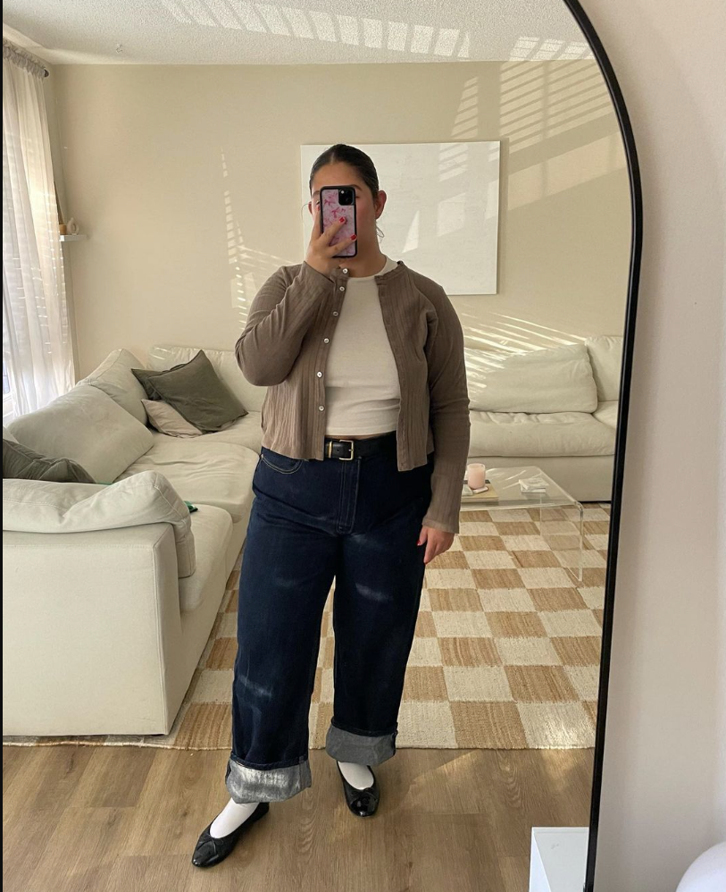 A plus size woman wearing Beige ribbed cardigan White fitted top Dark blue wide leg jeans Black belt with silver buckle Black ballet flats