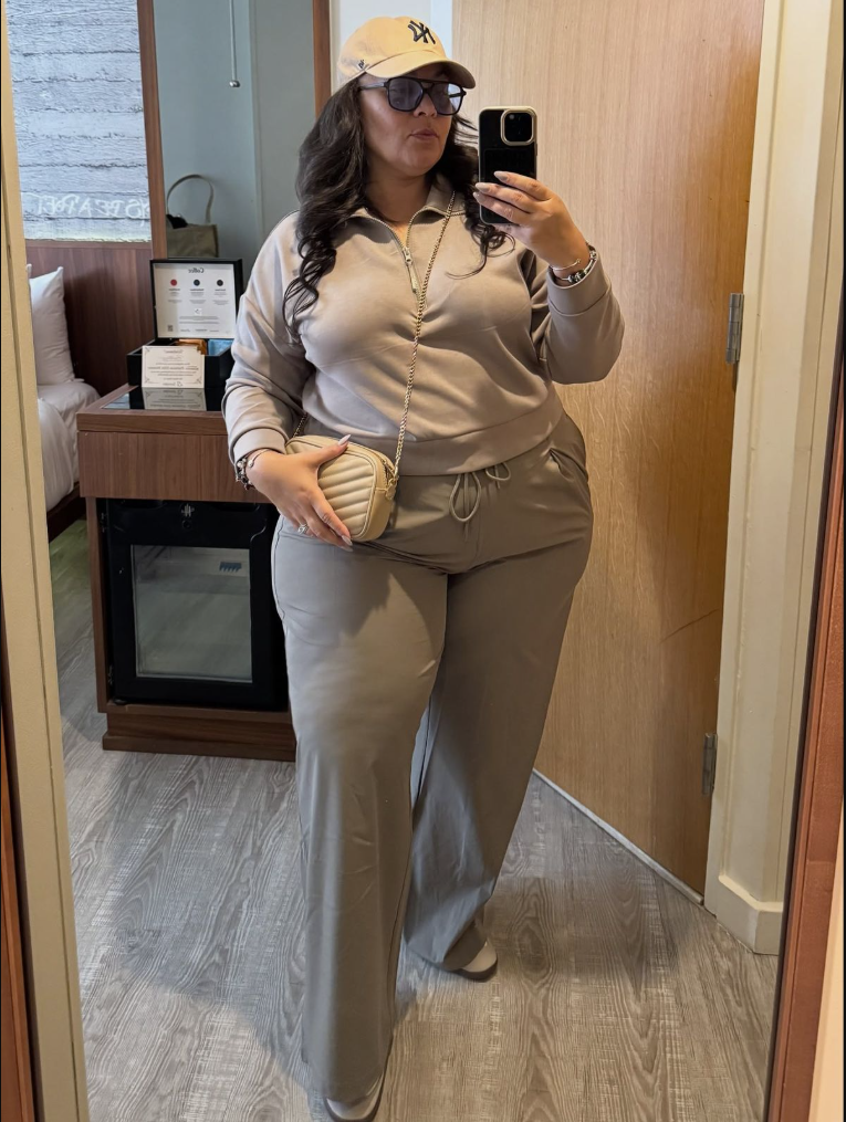 A plus size woman wearing Beige zip-up hoodie
Beige wide leg pants
Beige NY baseball cap
Sunglasses
Beige quilted crossbody bag