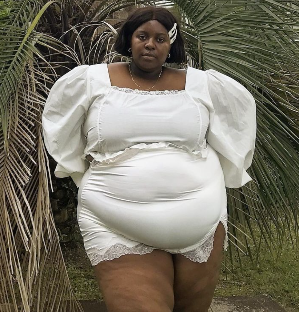 A plus size woman wearing White puff sleeve mini dress with lace trim Gold chain necklace Small hoop earrings